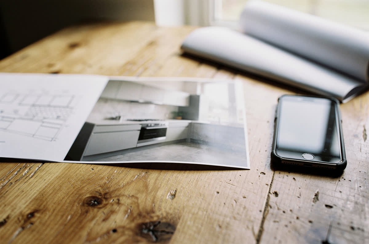 Printed photograph of a finished kitchen on a wooden table beside a phone and a folded kitchen plan