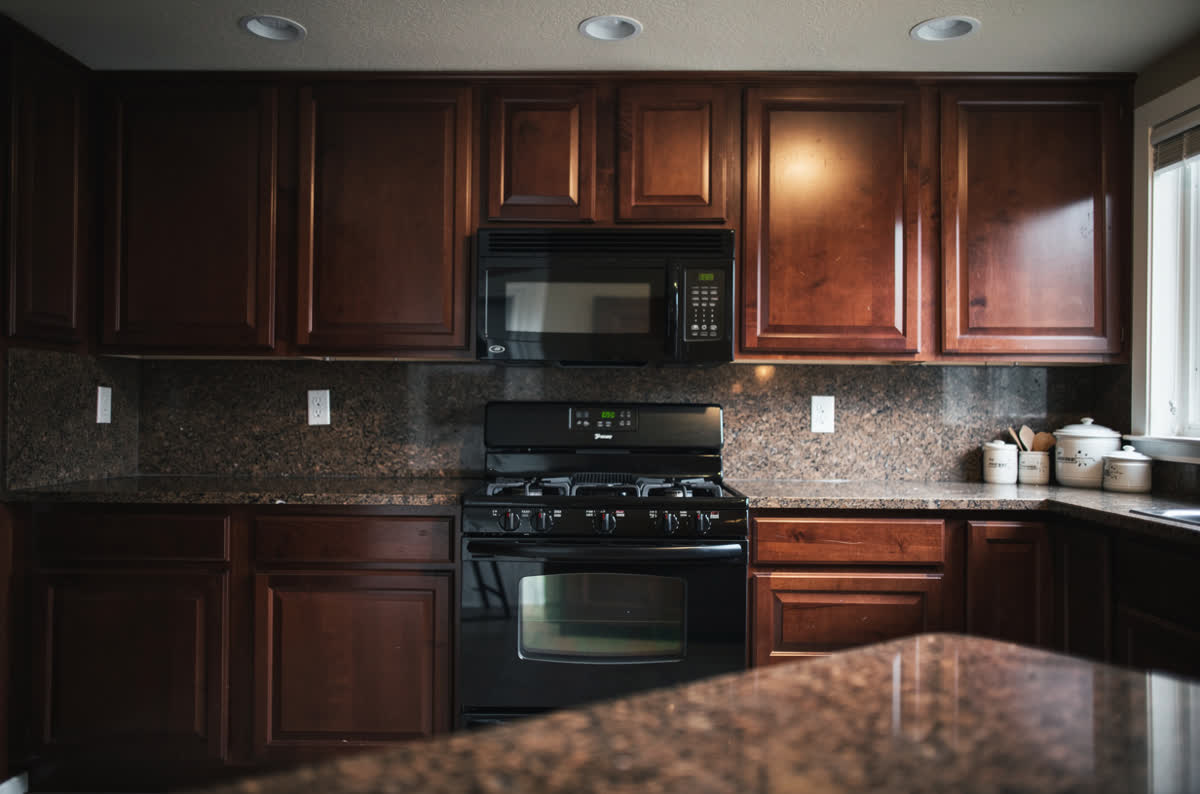 Dark kitchen with glossy cherry raised-panel cabinets, brown granite counters and a bulky over-range microwave