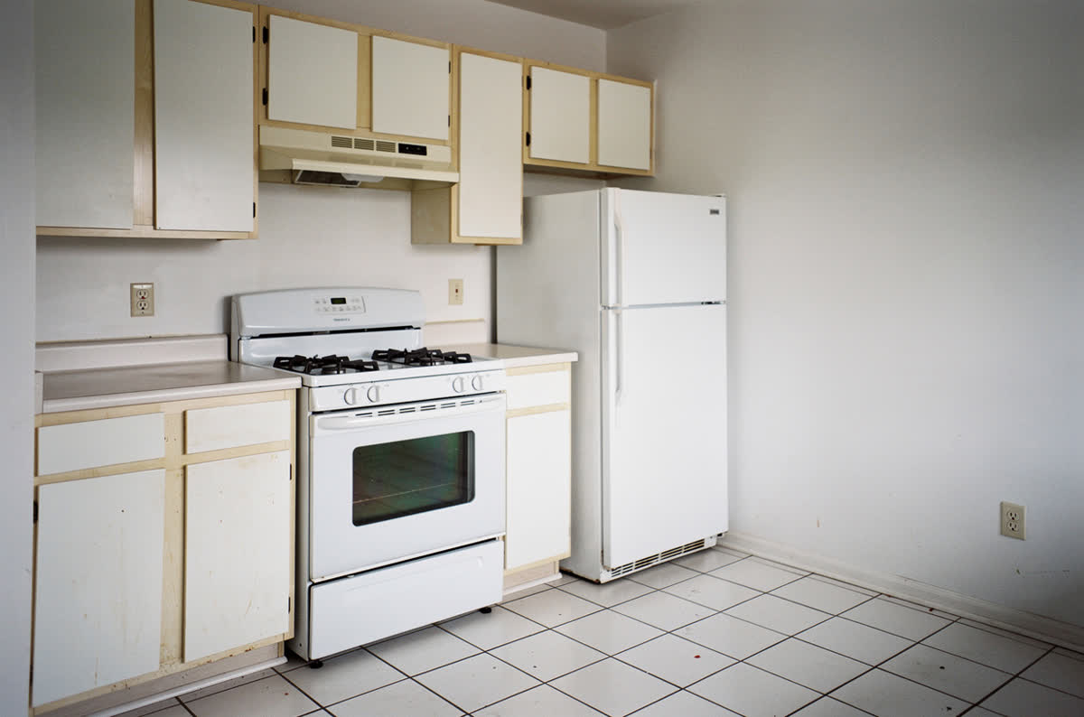Plain rental kitchen with flat white melamine cabinets, white laminate counters and bare walls