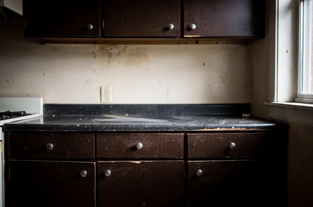 Dated kitchen with dark brown flat cabinet doors, a worn dark countertop and a bare wall