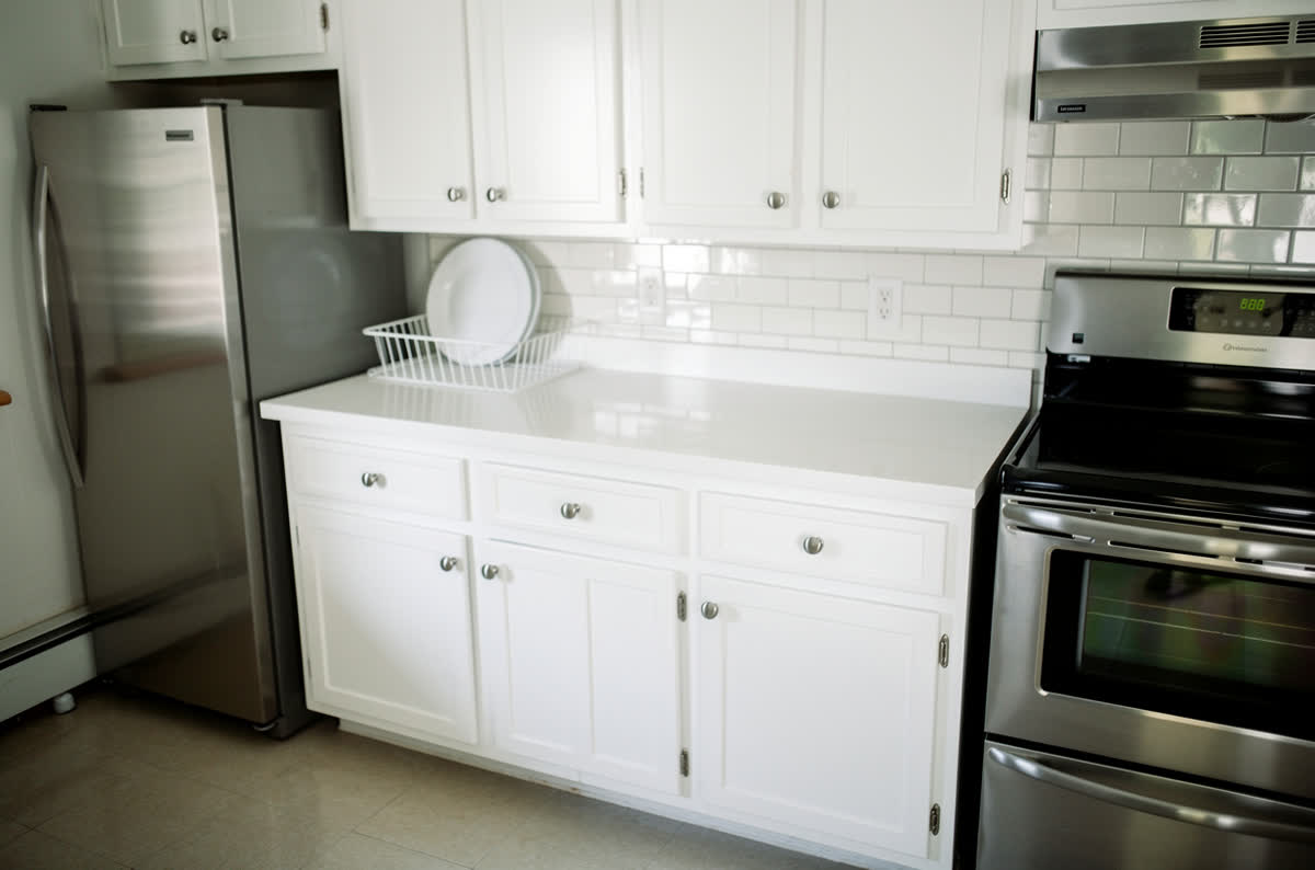 The same kitchen with white shaker doors, quartz counters, subway tile and new stainless appliances