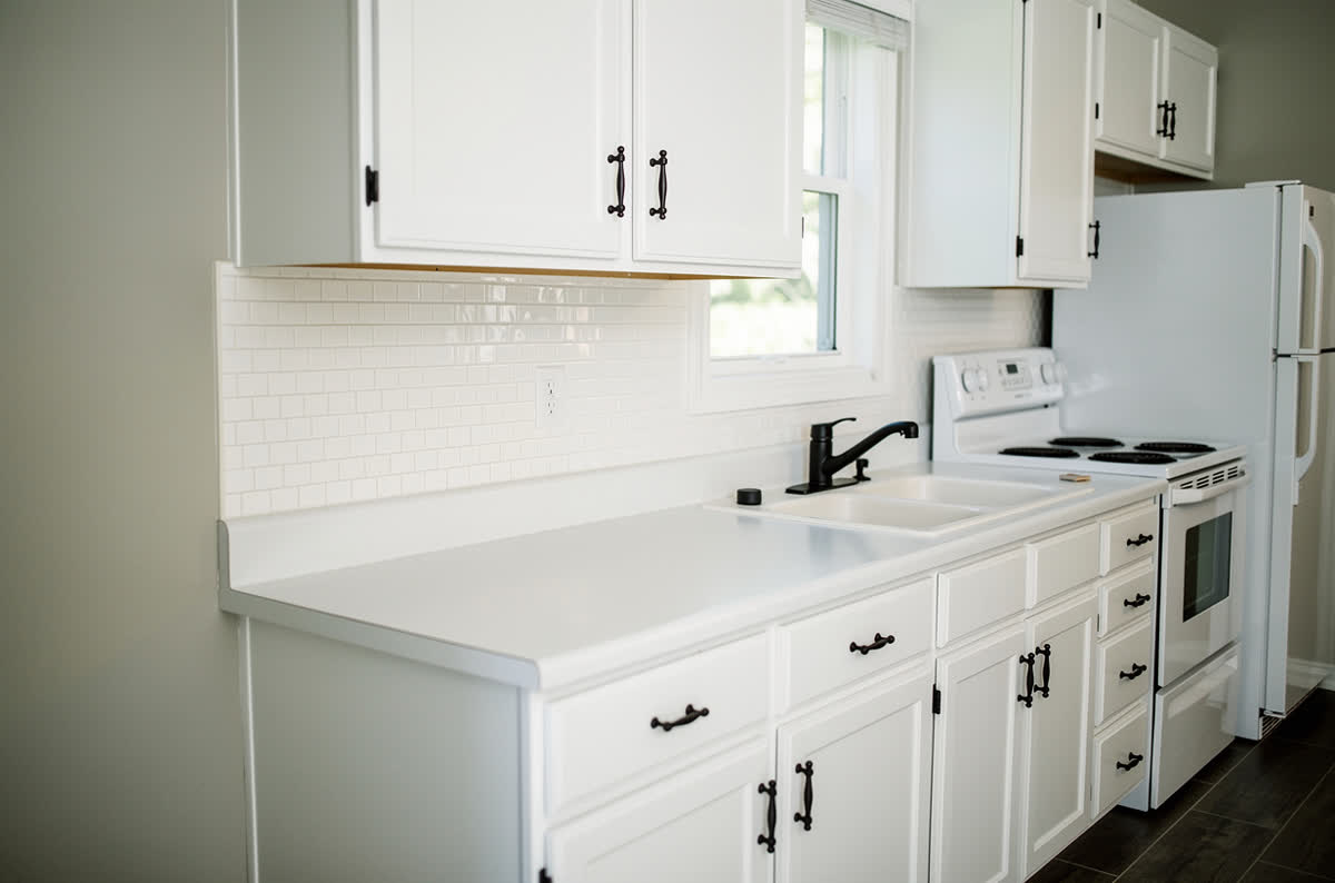 The same kitchen with painted white cabinets, matte black hardware, a peel-and-stick tile backsplash and a new faucet