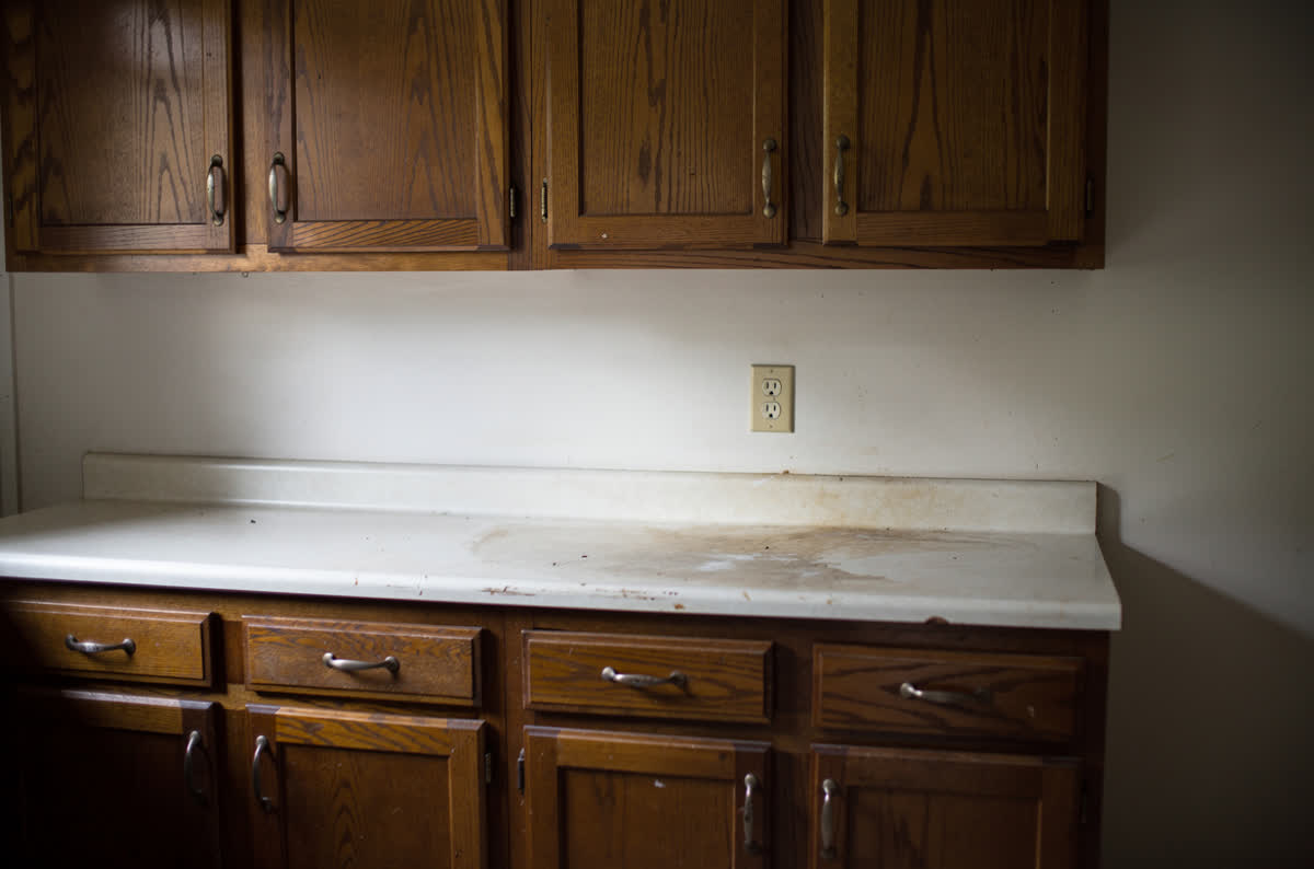 Dated kitchen with dark honey oak cabinets, a worn laminate countertop and a bare wall above the counter