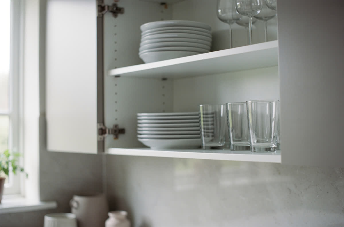 Upper cabinet doors removed to leave open shelving, the interiors painted white and holding plain plates