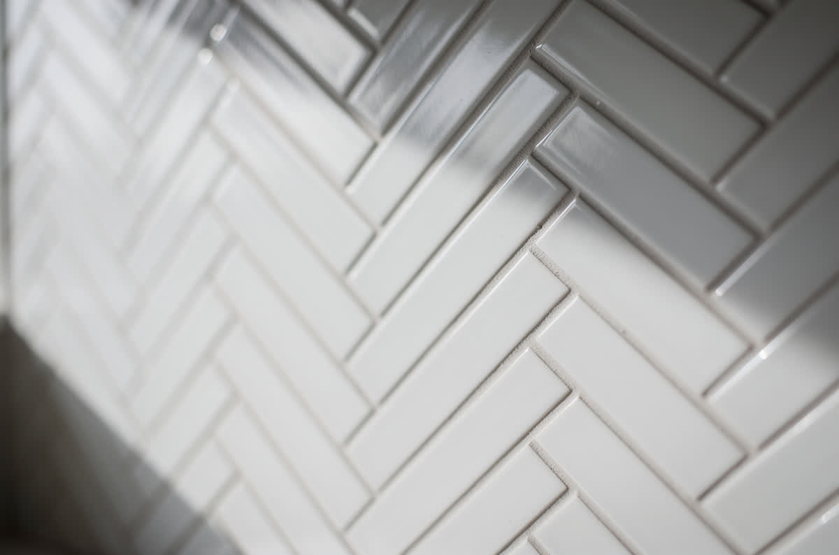 White subway tile laid in a herringbone pattern with pale gray grout