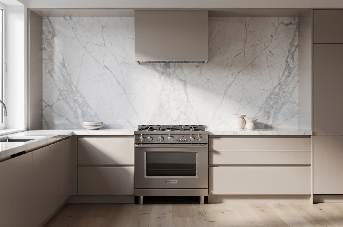 Full-height white marble slab backsplash rising behind a range, with no grout lines