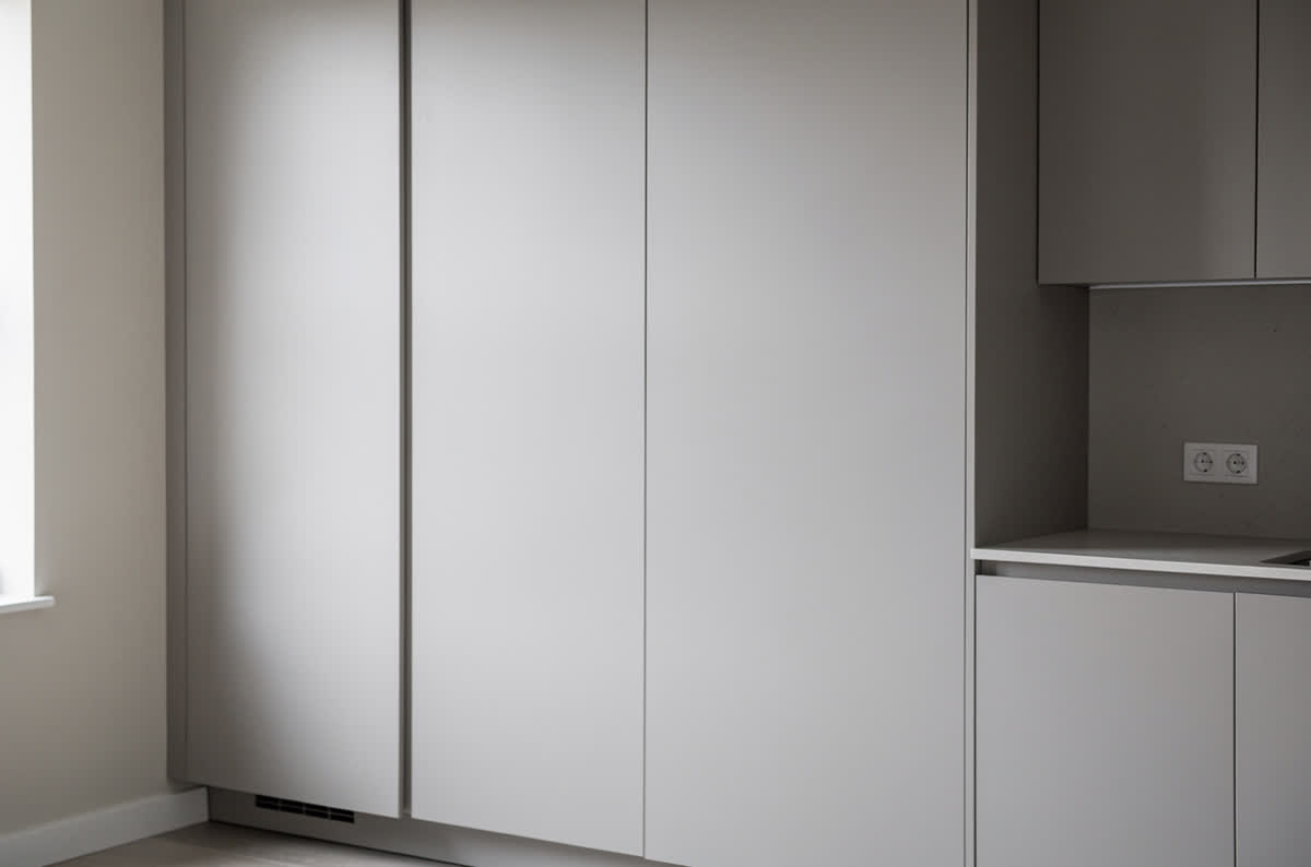 Smooth handleless flat slab cabinet doors in matte pale gray with no visible hardware