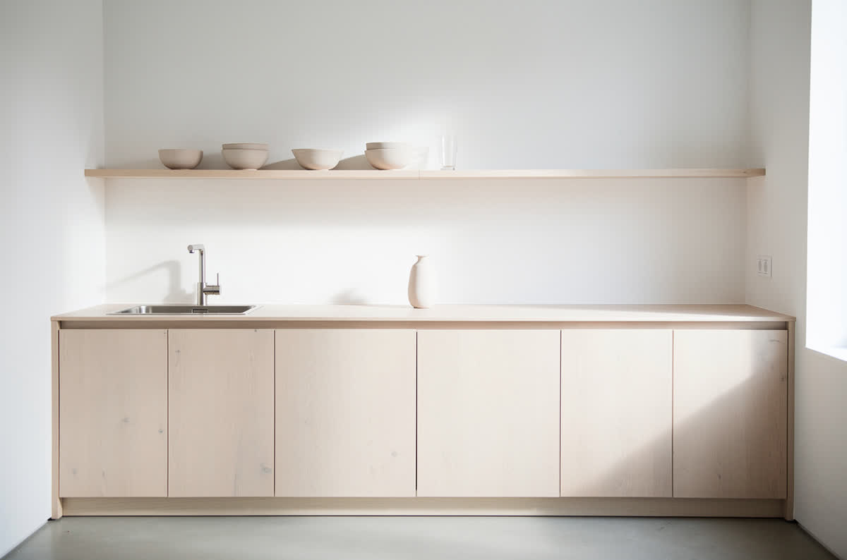 Small minimalist kitchen with one unbroken run of handleless pale oak cabinets