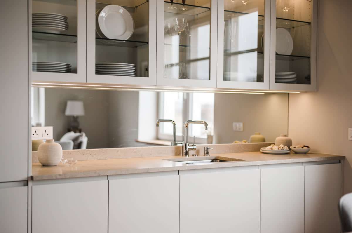 Small kitchen with a mirrored backsplash reflecting the window and glass-fronted cabinets