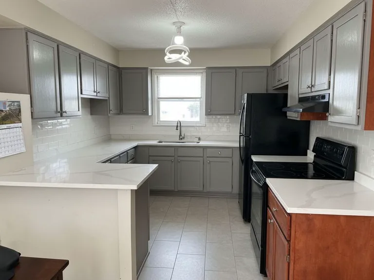 The same kitchen with gray painted cabinets, white quartz counters and a white subway backsplash