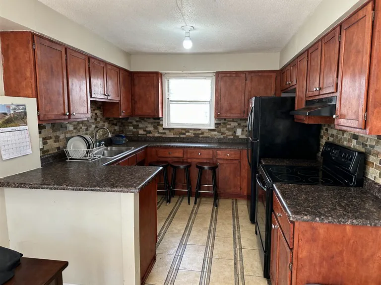 Kitchen with cherry cabinets, dark speckled laminate counters, a mosaic backsplash and a peninsula with three stools