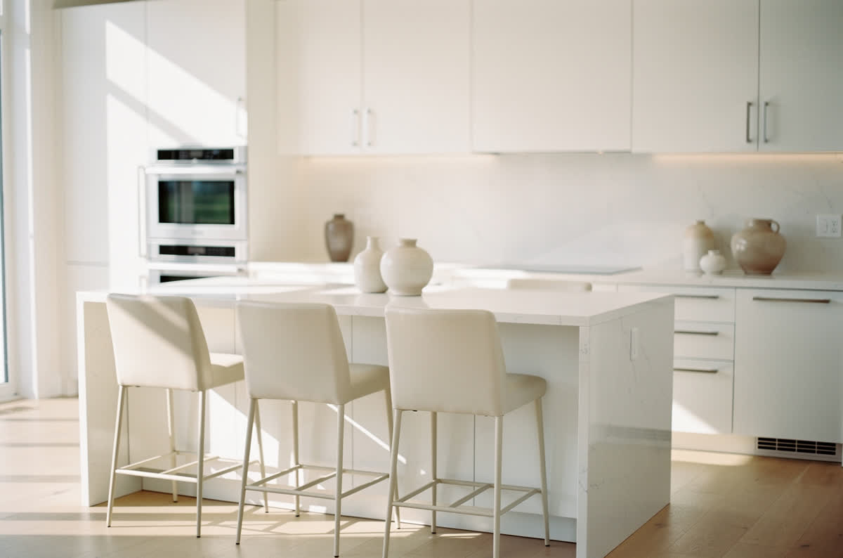 All-white kitchen with white cabinets, white countertops and cream accents in full daylight