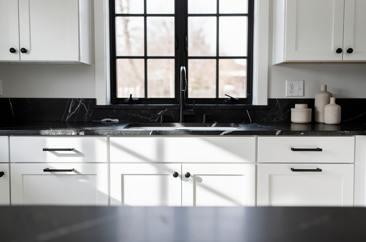 White kitchen with matte black hardware, black granite counters and a black-framed window