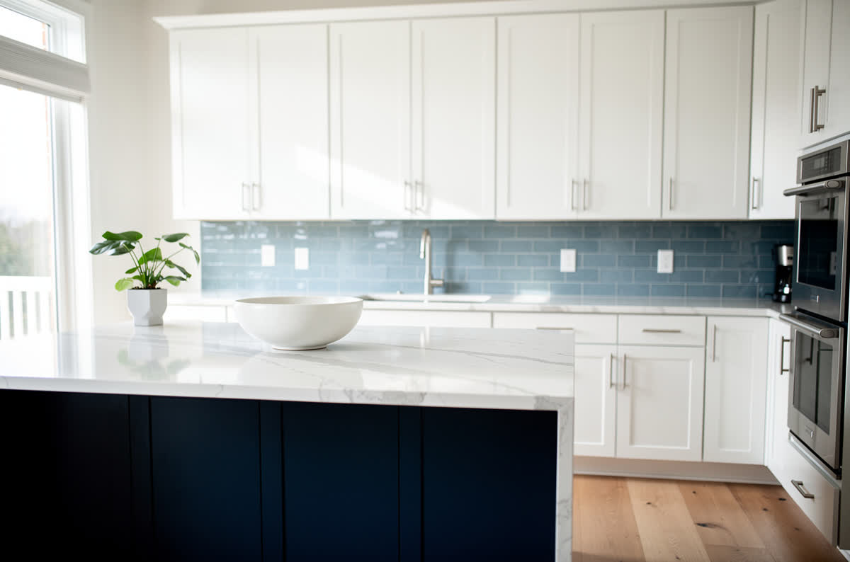White kitchen with a deep navy blue island and a soft blue tile backsplash
