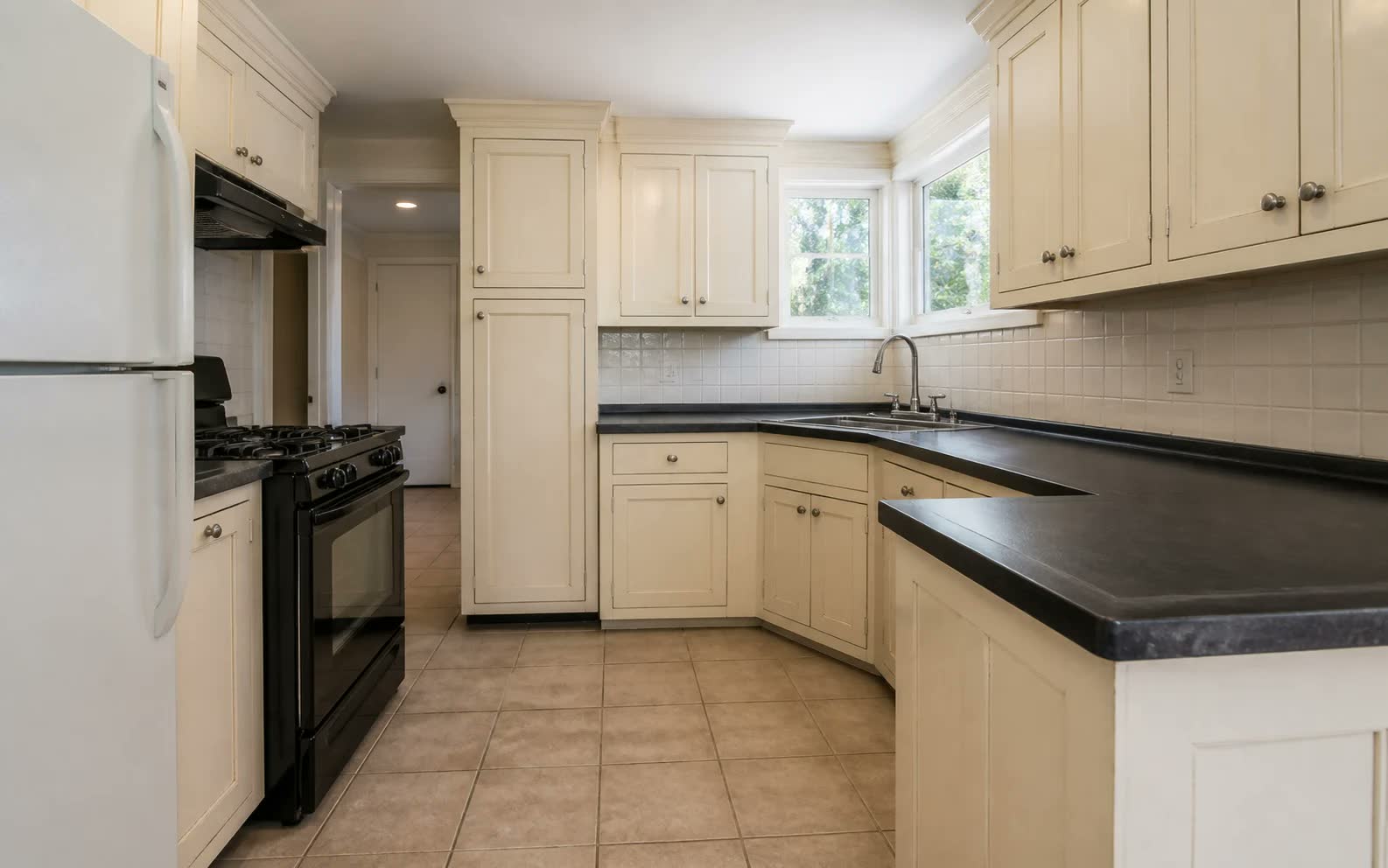 A dated kitchen with cream raised panel doors, black granite countertops and a black range