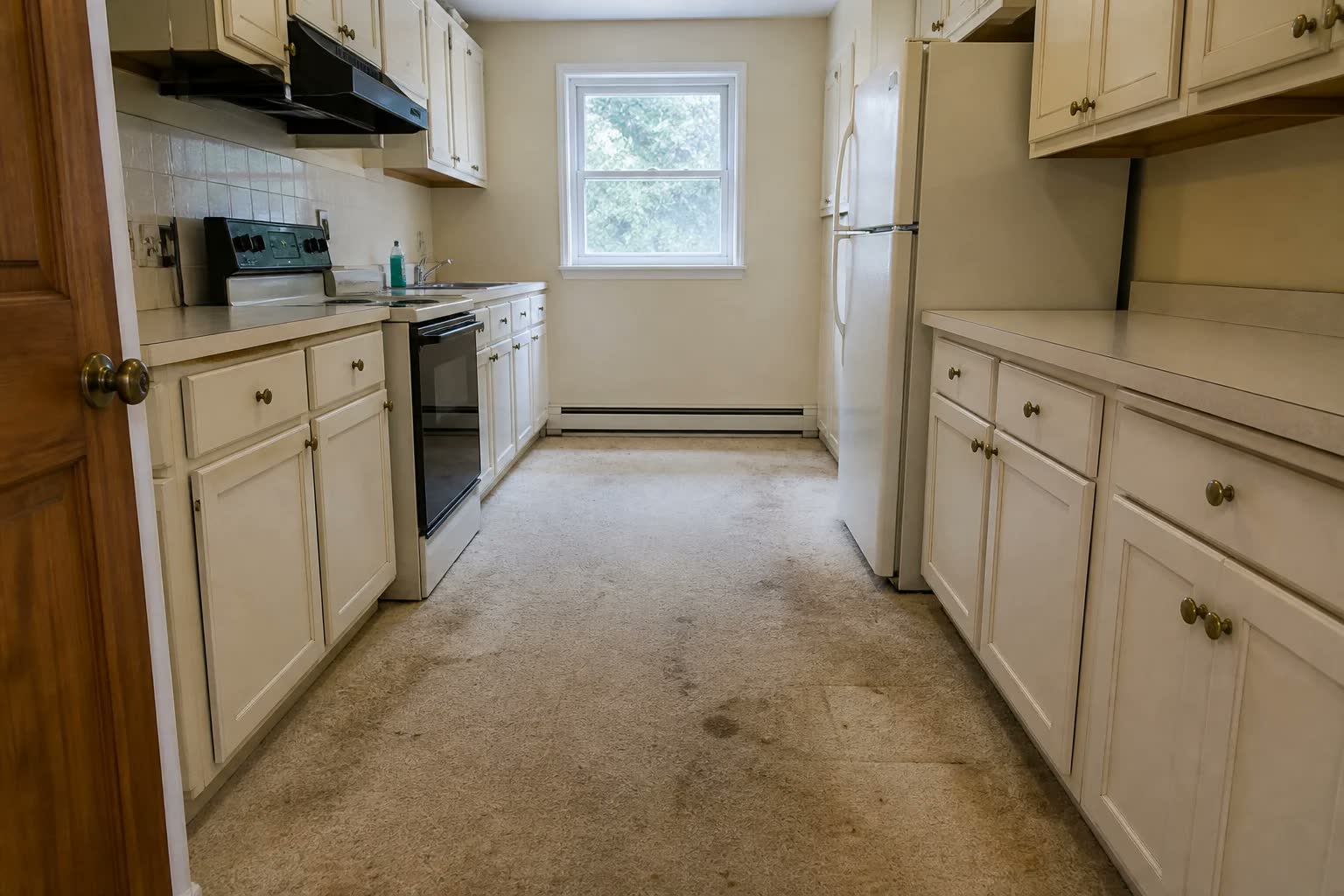 A cream galley kitchen with a worn, stained beige carpet on the floor